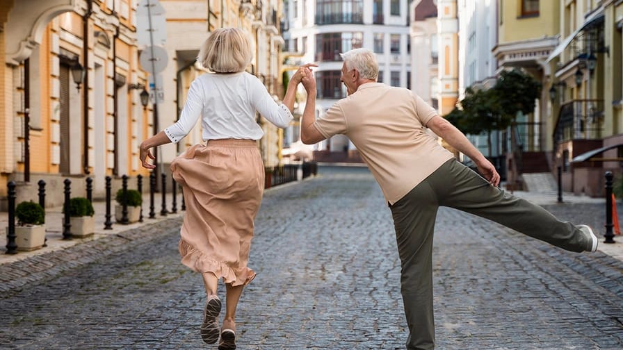 An old couple walks along a street while dancing